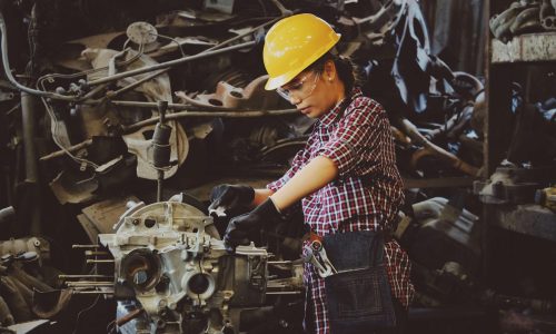 Woman engineer wearing safety gear, working on machine repair in an industrial setting.